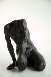 frontal view of a sculpture of a male nude sitting on his knees