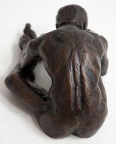 dorsal view of a bronze sculpture of a male nude sitting with his head on his knee