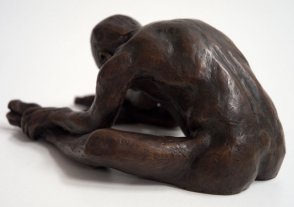 sinister lateral dorsal view of a bronze sculpture of a male nude sitting with his head on his knee